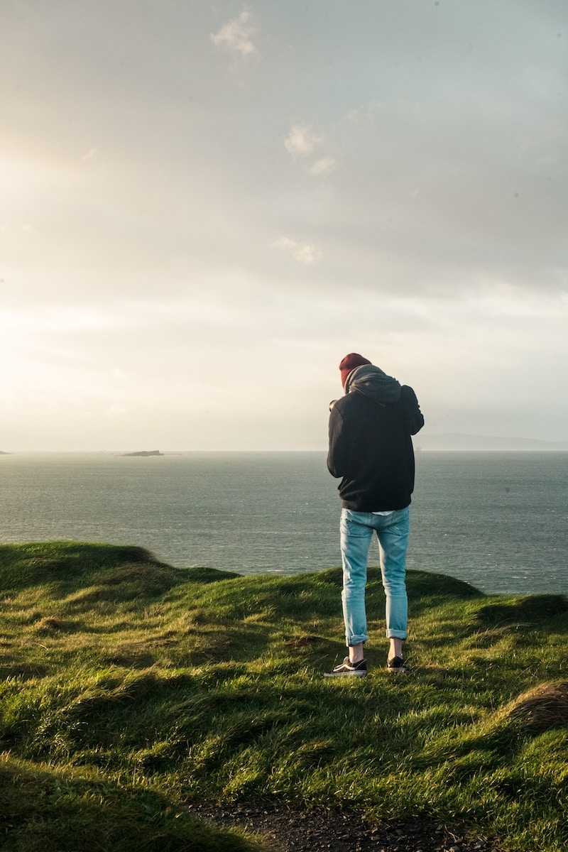 man in black jacket and blue denim jeans standing on green grass field near body of with near near near